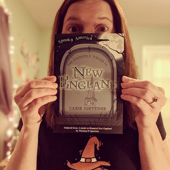 Image is a photo of Carie Juettner holding a book titled The Ghostly Tales of New England.