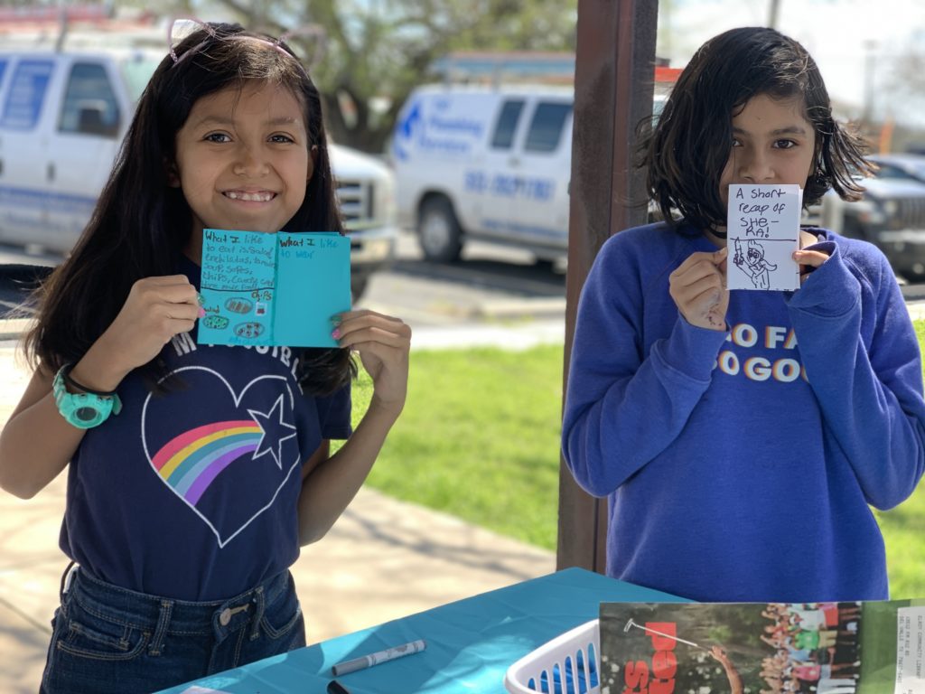 Two girls holding up their small handmade zines.