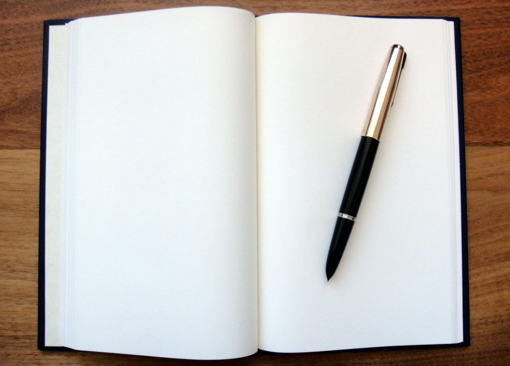 A black journal with blank white pages and a fountain pen sitting on top. 