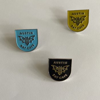 Image: 3 metal pins featuring ABC's logo with a bat and the words Austin Bat Cave. One pin is yellow-gold, one is powder blue, and one is black.