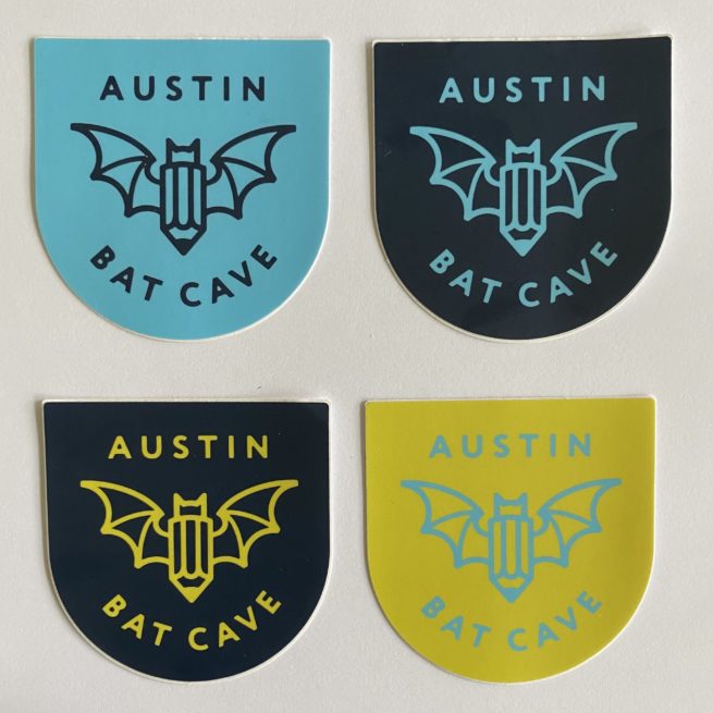 Image: 4 stickers with ABC's logo that features a bat and the words Austin Bat Cave. Each sticker is a different. Colors include powder blue background with dark blue logo; dark blue background with powder blue logo; dark blue background with yellow-gold logo; and yellow-gold background with powder blue logo.