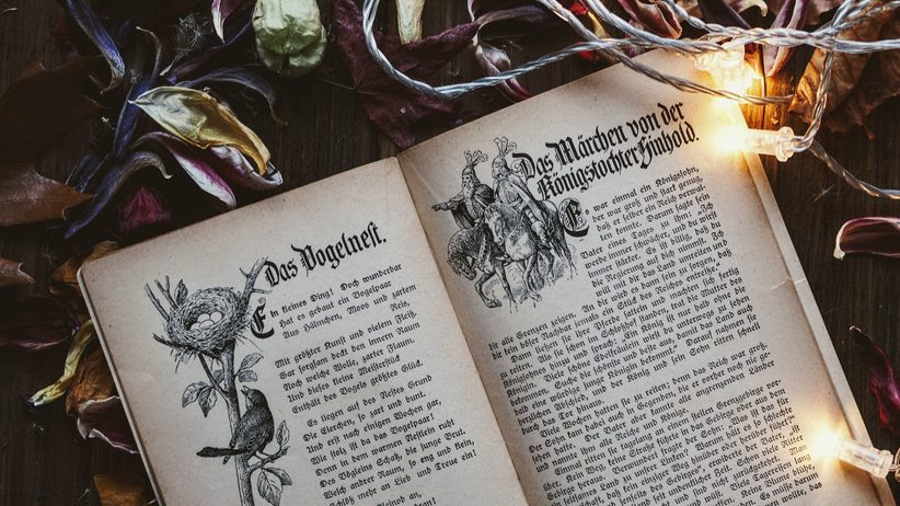An old book of fairy tales in German on a wooden table surrounded by lights and leaves. 