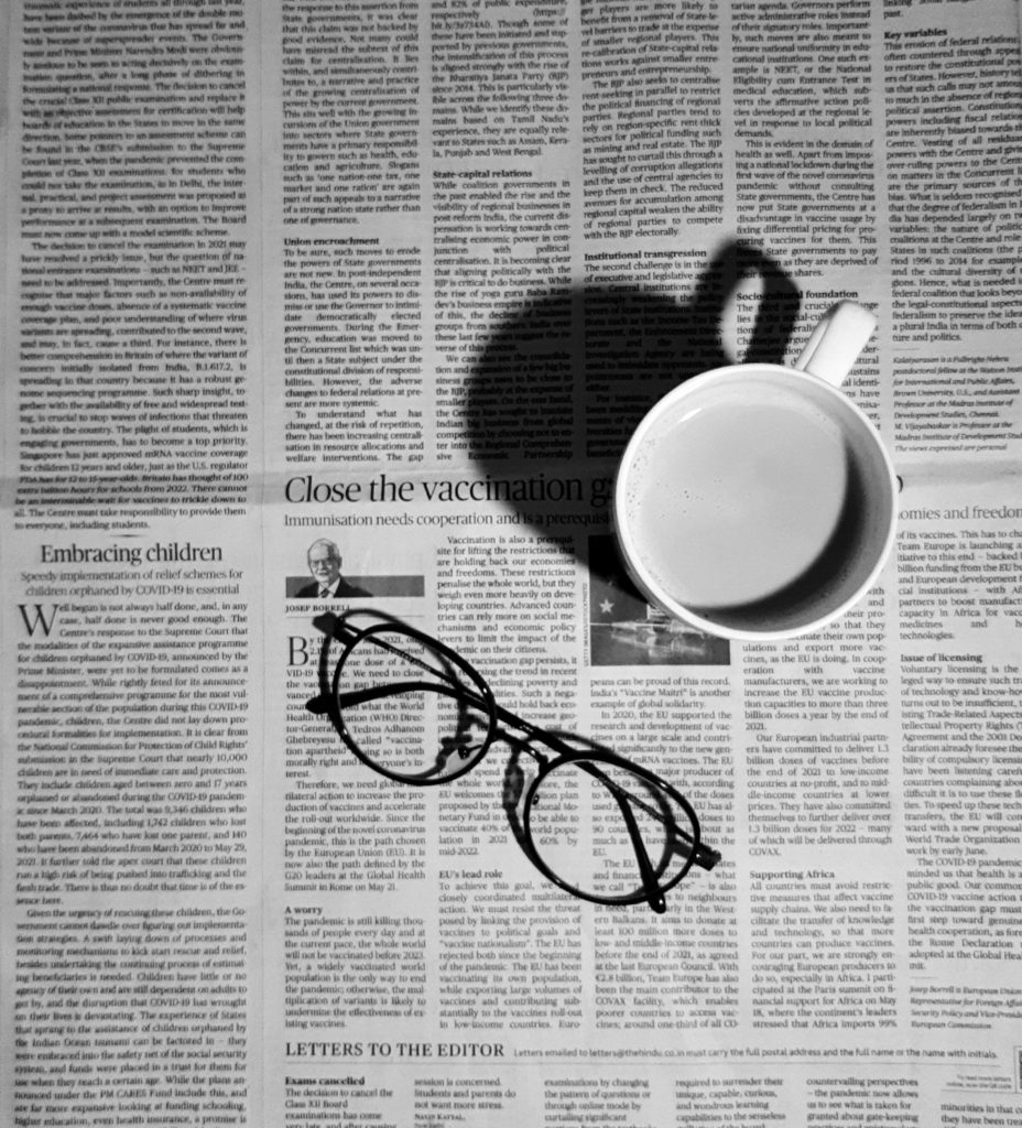 A newspaper spread on a table in black and white with a white coffee cup and black framed glasses sitting on top of it. 