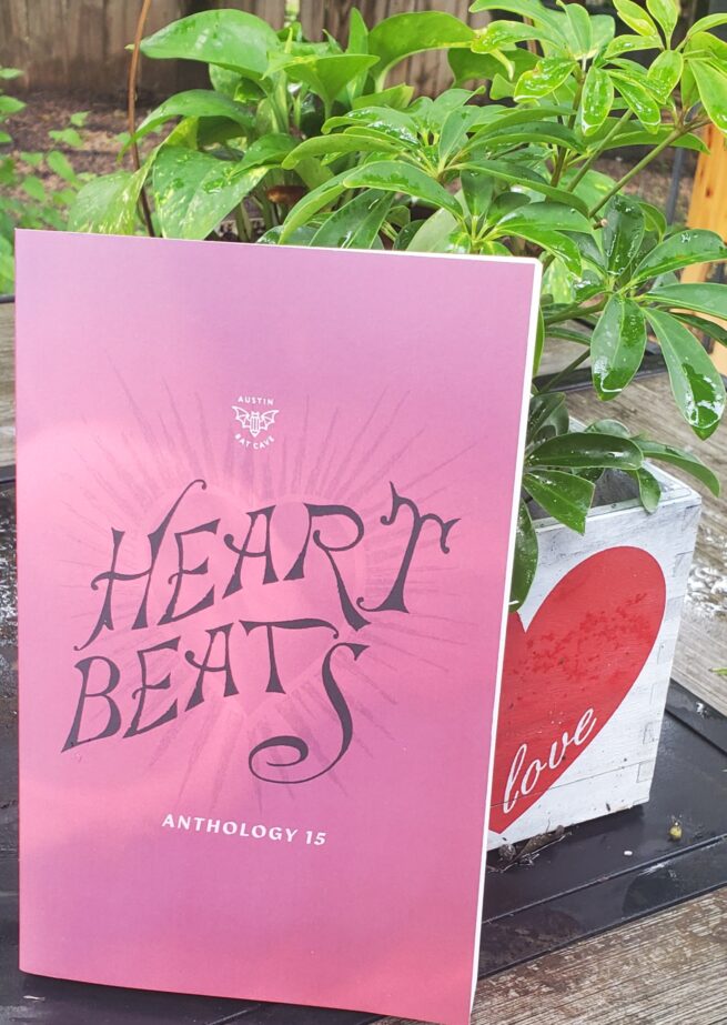 The Heart Beats anthology rests against a plant in a white pot. The book cover features a red gradient and the title in black cursive.