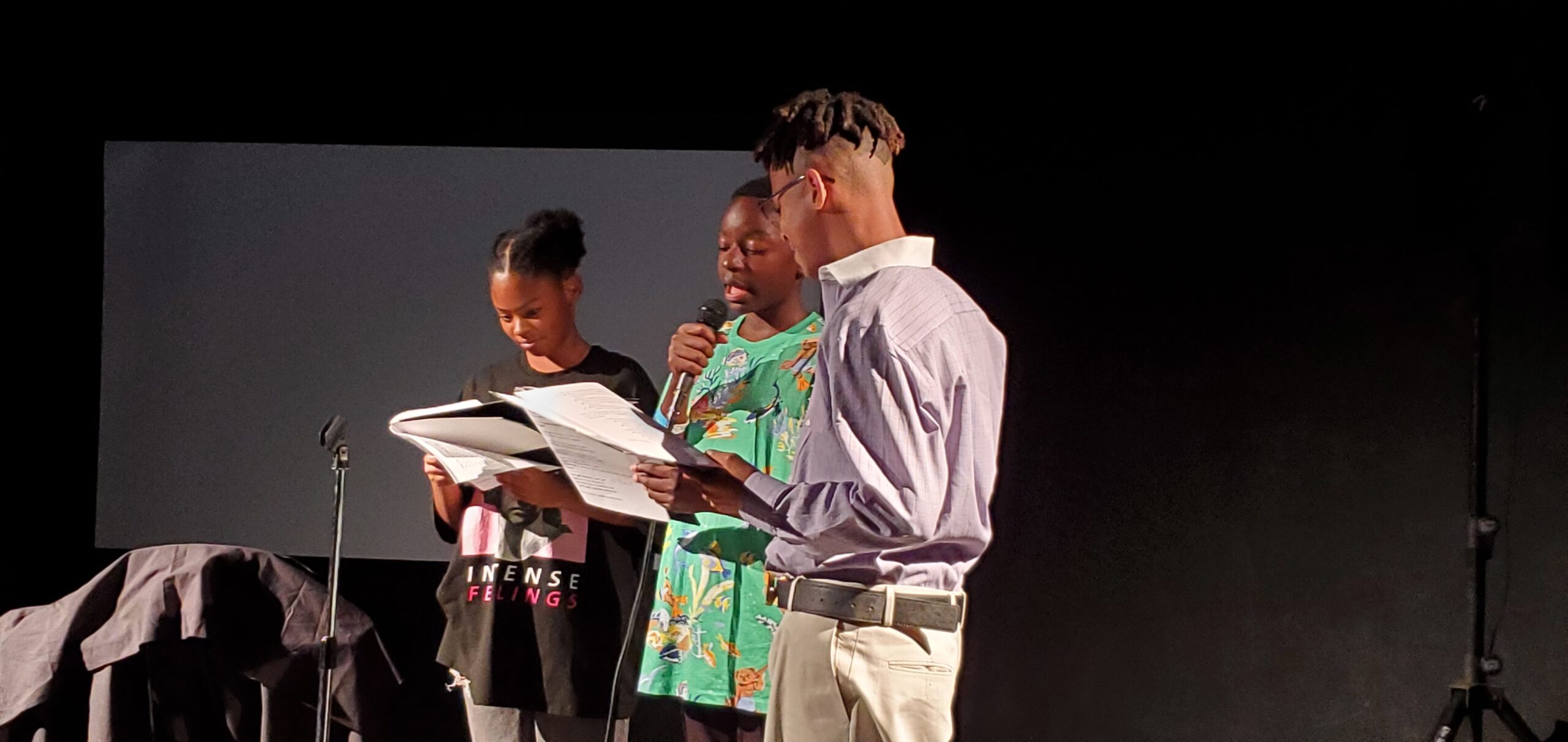 Three youth poets in the Courageous Cadence summer program perform their poetry at the Vortex Theater with a microphone