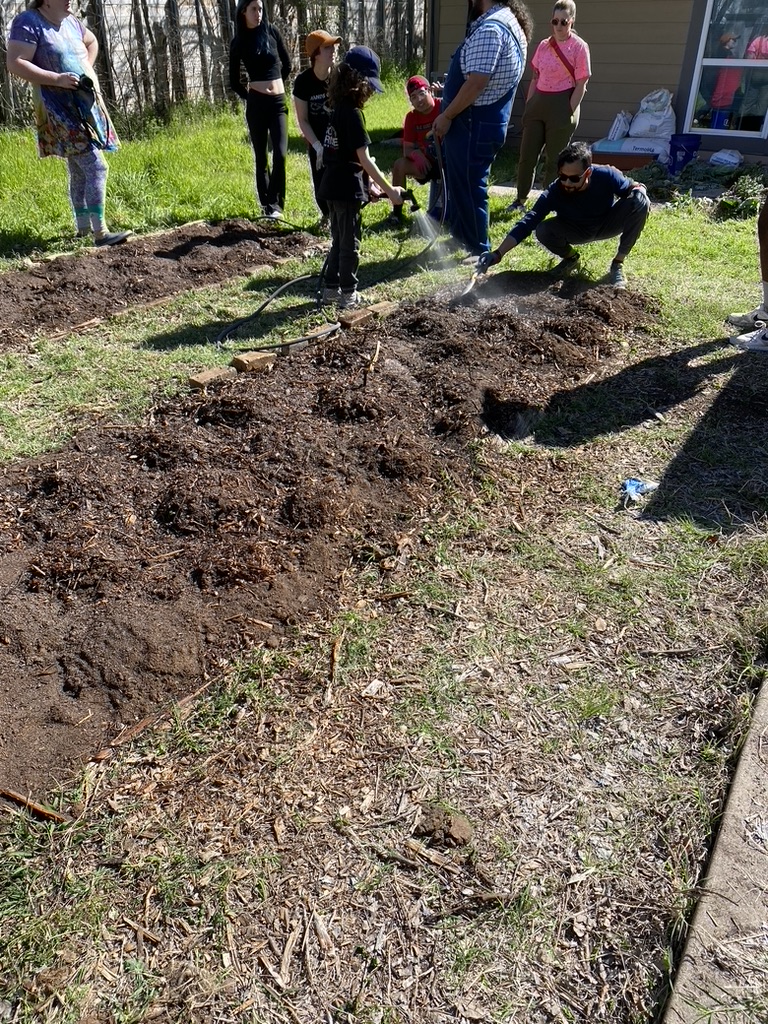 A group of kids and adults watering newly planted corn in a freshly tilled garden. 