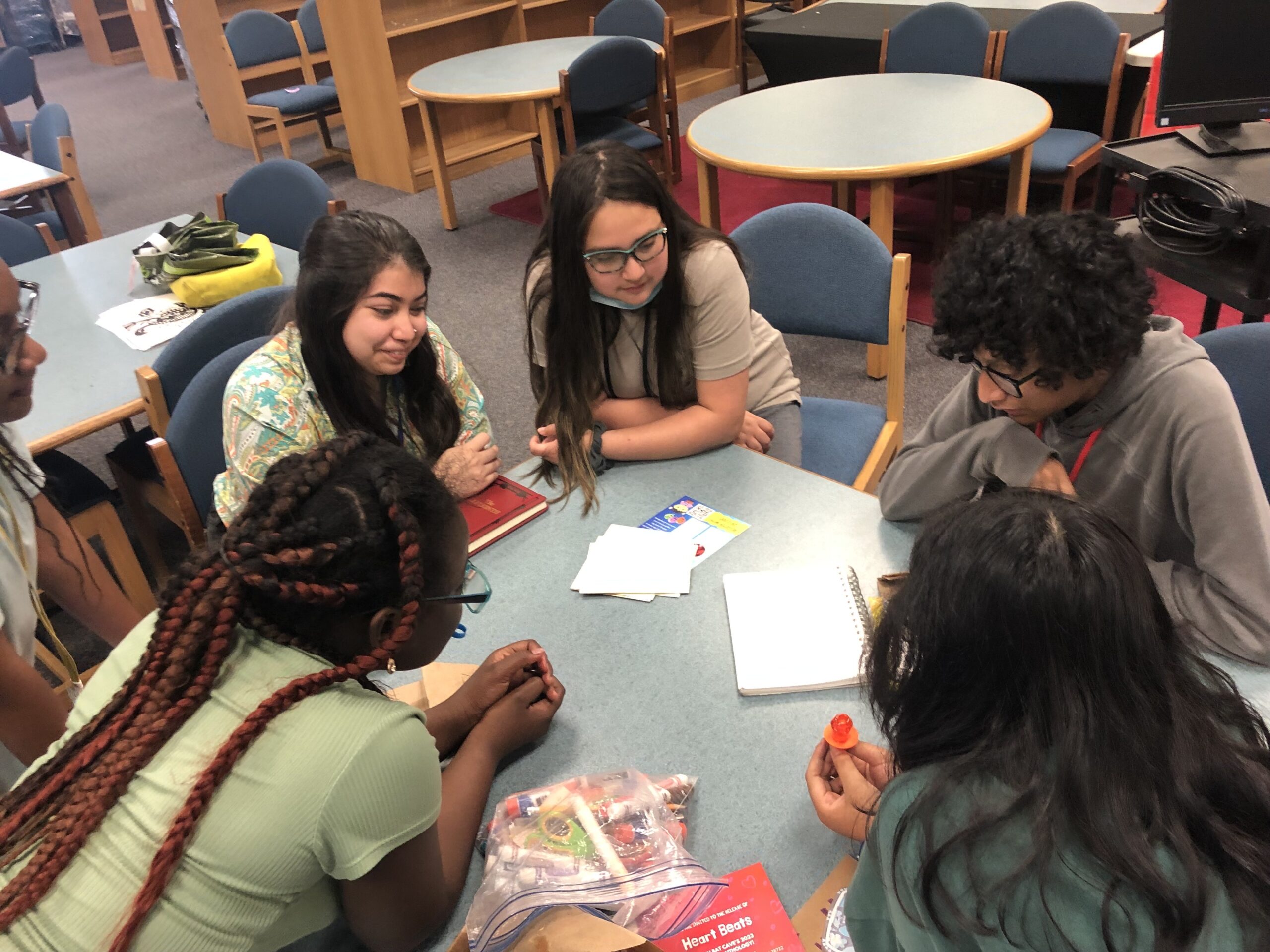 Students sit around a round library table writing and discussing with their instructor. 